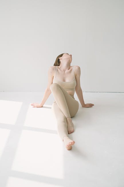 A woman in a red top performing a yoga pose in a spacious light-filled studio.